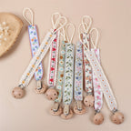 Beech Wood Dummy Clip, Embroidered Soother Holder, shown on a bed