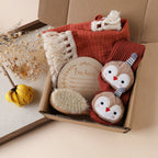 Newborn Gift Box, Tassel Comforter, Socks and Brush, shown on a bed