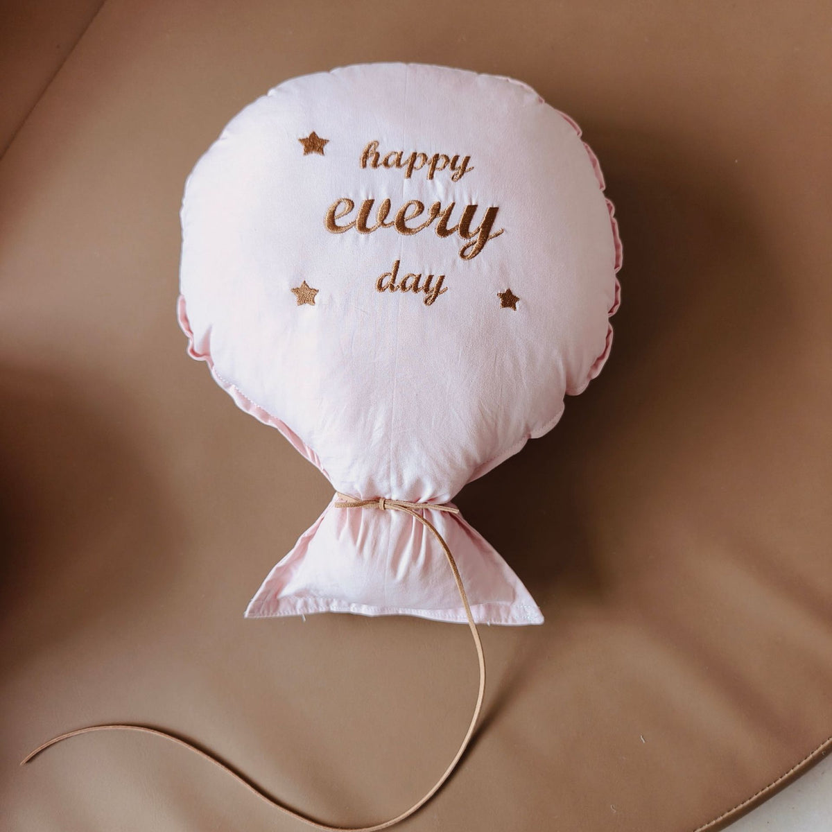 Balloon-shaped nursery cushion with an embroidered message on a nursery shelf – Pink, Happy Every Day