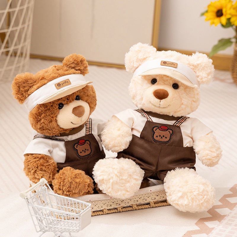 Teddy bear in brown dungarees with checked straps and white visor – view 6 of 7