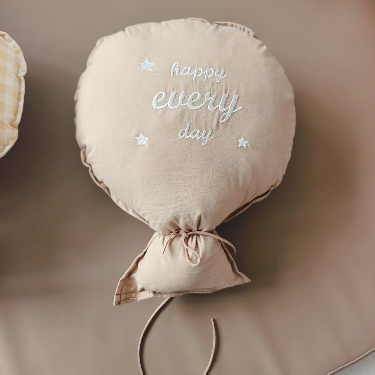 Balloon-shaped nursery cushion with an embroidered message on a nursery shelf – Mocha, Happy Every Day
