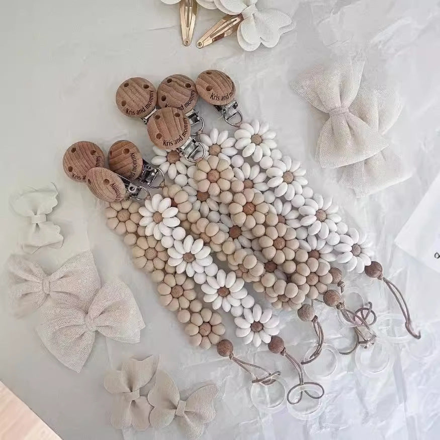 Silicone Daisy Dummy Clip, Beaded Soother Holder, shown on a bed