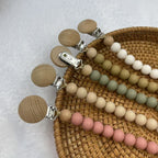 Silicone and Beech Dummy Clip, Beaded Soother Chain, shown on a bed
